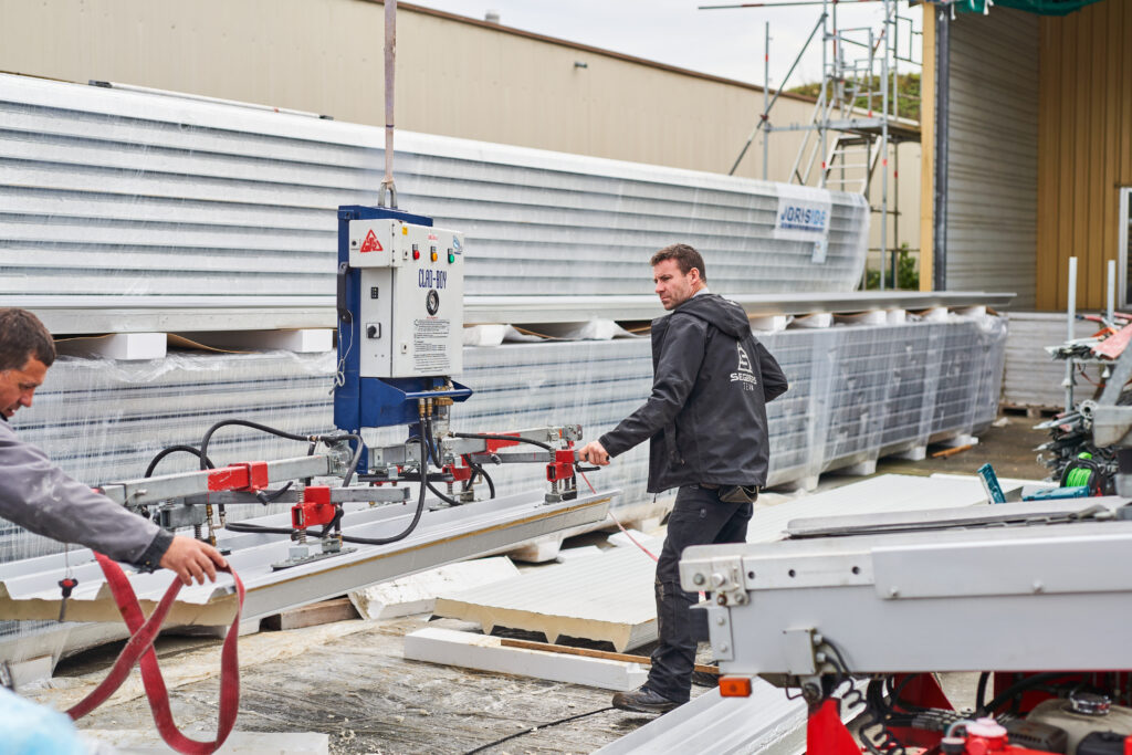Arbeiter bedienen Maschine zum Schneiden von Metallplatten im Freien. Baustelle im Hintergrund.